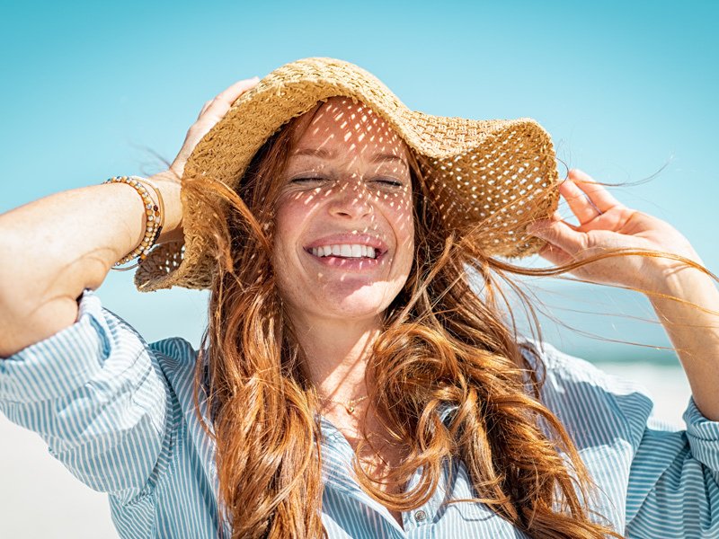Life Extension, a red-haired woman wearing a sun hat smiling and looking energized on a sunny day