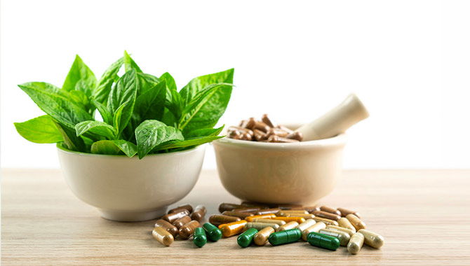 Two white bowls filled with green leaf salad and supplement capsules, on a table with more capsules